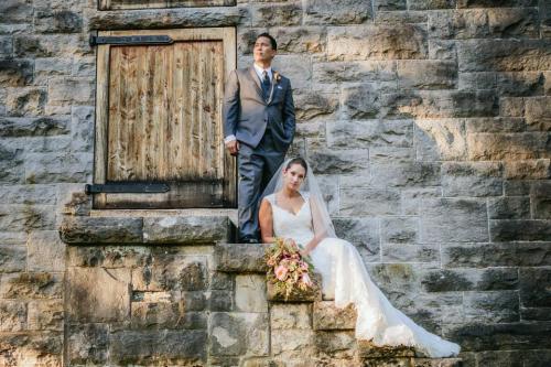 bride and groom posing in front of a stone house